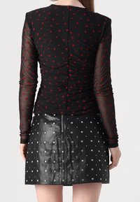 Svart långärmad topp med röd hjärtmönster och samlad design; i kombination med en svart läder mini kjol med silvernitar och dragkedja.