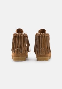 Semišové kotníkové boty světle hnědé barvy s dlouhými třásněmi na zadní straně, texturovanou podrážkou a dekoračními tkanými prvky na vrchní části.