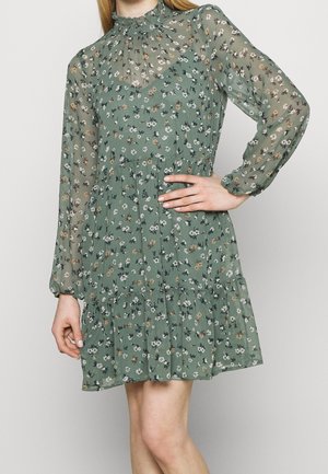 Grünes Blumenmusterkleid mit hohem Rüschkragen, durchsichtigen langen Ärmeln und gestuftem Rock, der kleine weiße und braune Blumenmuster aufweist.