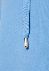Tessuto di felpa blu chiaro con un cordoncino intrecciato che termina con un dettaglio in metallo argentato lucido.