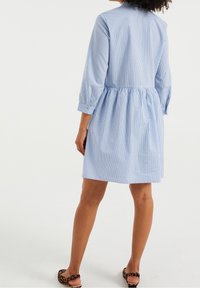 Sininen ja valkoinen raidallinen paitamekko, jossa on kolme neljäsosaa hihat, rypistetty vyötärö ja rento leikkaus, yhdistettynä kuvioituihin litteisiin sandaaleihin.