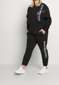 Sudadera negra y jogging de algodón suave. Presenta un logo blanco en el pecho y en los pantalones. Corte clásico con puños acanalados.