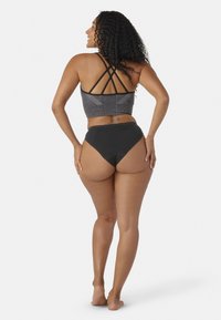 Mutande nere a vita alta abbinate a un crop top a motivi neri e grigi con spalline incrociate, viste da dietro.