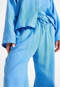 Modrý, textúrovaný súbor loungewear pozostávajúci z košele na gombíky a nohavíc na šnúrku, s mierne uvoľneným strihom a jemným gradientným odtieňovaním.