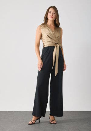 Satin wrap jumpsuit featuring a taupe bodice, black wide-leg trousers, and a tied waist detail. Black high-heeled sandals complement the outfit.