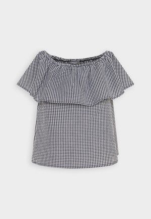 Το τοπ με ανοιχτούς ώμους σε μαύρο και άσπρο καρό σχέδιο, διαθέτει βολάν στο λαιμό και κοντά μανίκια. Είναι κατασκευασμένο από ελαφρύ ύφασμα.