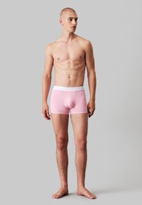 Boxer in jersey rosa chiaro con elastico bianco in vita, caratterizzati da una vestibilità aderente e una texture liscia. Il design è semplice e minimalista.