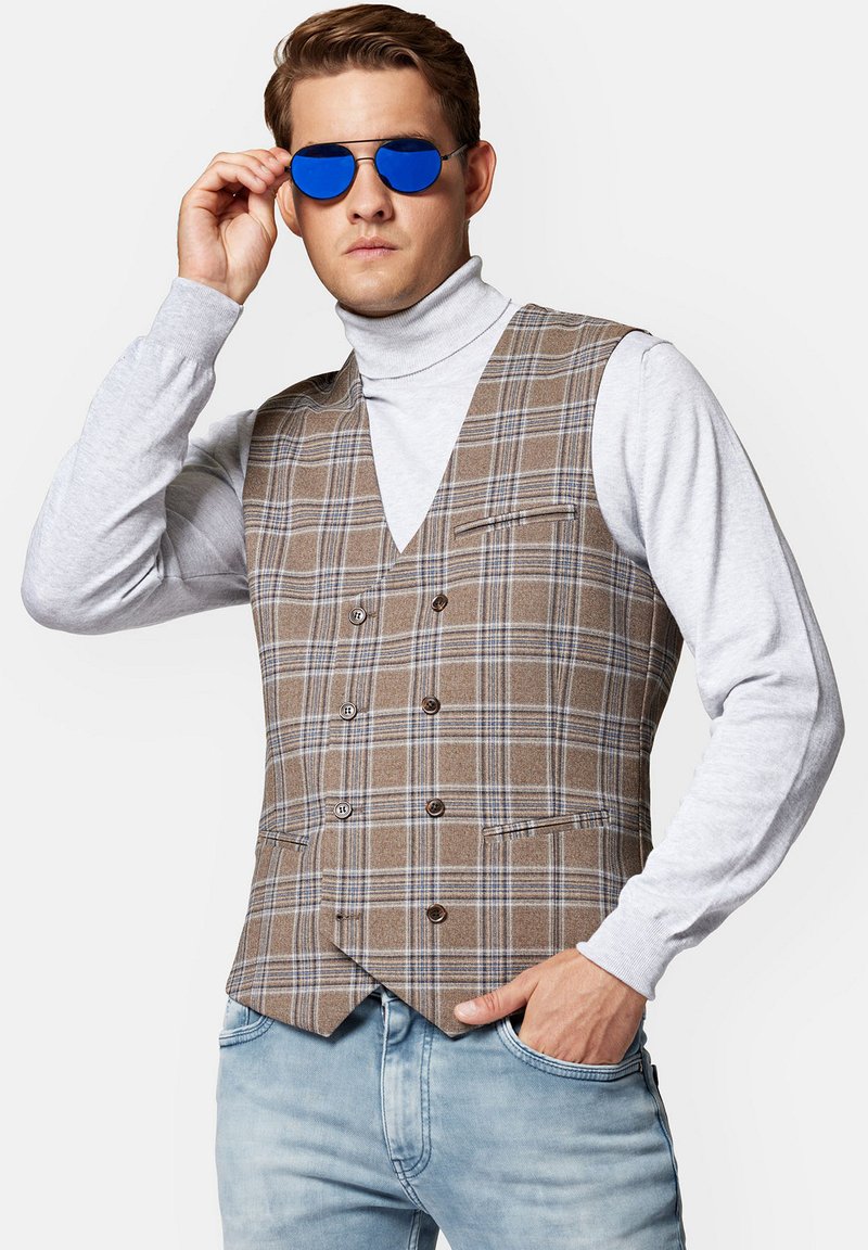 Brązowa kamizelka w kratę z niebieskimi akcentami, podwójnie zapinana, z dwiema przednimi kieszeniami, w połączeniu z szarym golfem i niebieskimi okularami przeciwsłonecznymi.