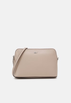 Beige DKNY crossbody bag with a smooth texture, silver logo plate, and a matching adjustable strap with chain detail on a white background.