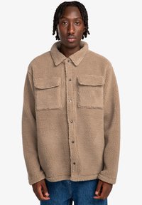 Brown fleece jacket with a collared neck, snap buttons, and two front pockets. Soft texture with a loose fit.