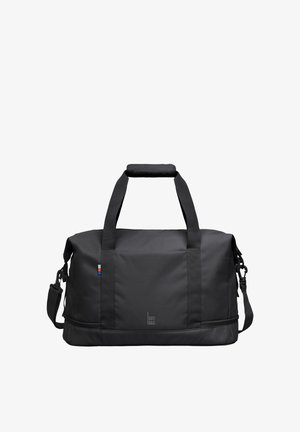 Schwarze rechteckige Duffel-Tasche mit zwei Griffen, einem gepolsterten Schulterriemen, kleinem farbigem Etikett und "GOT BAG" Logo vorne in der Mitte.