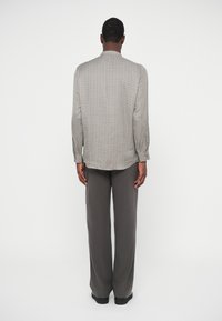 Πουκάμισο σε ανοιχτό γκρι χρώμα με ζιγκ-ζ�αγκ μοτίβο, διαθέτει γιακά μαανταρίνι, μακριά μανίκια και καμπυλωτό στρίφωμα. Συνδυασμένο με γκρι παντελόνια σε φαρδιά γραμμή.