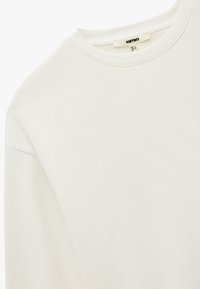 Creme sweatshirt med rund halsudskæring, ribbede manchetter og blød tekstur. Har et mærkebanner syet på halsudskæringen.