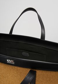 Czarna i brązowa torba pleciona z czarnymi skórzanymi uchwytami i wykończeniem, z srebrnym logo "KARL LAGERFELD" na zewnątrz.