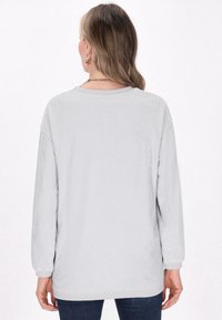Maglietta grigia a maniche lunghe con texture a coste, scollo rotondo e vestibilità ampia, abbinata a pantaloni di jeans scuri.