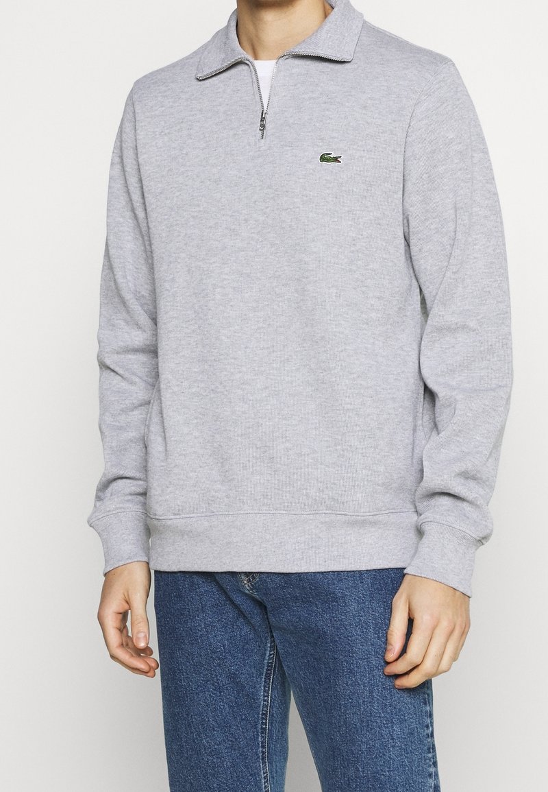 Grauer Sweatshirt mit Reißverschluss aus weichem Stoff, mit Kragen und kleinem grünem Logo. Stilvoll ergänzt durch gerippte Bündchen und Saum.
