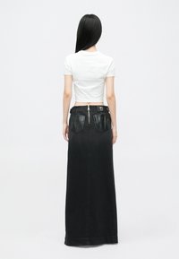 Fekete farmer maxi szoknya bőr díszítésű zsebekkel és hátsó cipzárral, egy fehér cropped pólóval párosítva.