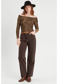 Bronzen top zonder schouders met sprankelende textuur, gecombineerd met hoge taille, bruine wijde jeans en een bruine riem. Bruine enkellaarsjes maken de look compleet.