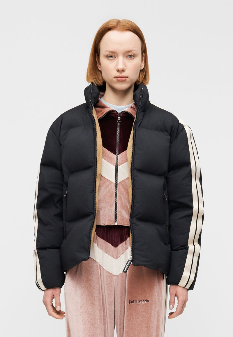 Μαύρο φουσκωτό μπουφάν με ψηλό για κά, κλείσιμο με φερμουάρ και μπεζ λεπτομέρειες. Διαθέτει οριζόντιες ρίγες στα μανίκια και καπιτονέ υφή.