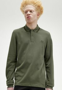 Polo shirt a maniche lunghe di color verde oliva realizzato in tessuto testurizzato, presenta strisce scure a contrasto sul colletto e un piccolo emblema sul petto.