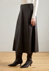 Brun läder midi-kjol med en utsvängd design. Har en sidodragkedja och diskret sömdetaljering. Stylande med svarta spetsiga ankelstövlar.