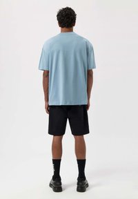Himmelblaues Baumwoll-T-Shirt mit lockerer Passform, kurzen Ärmeln und Rundhalsausschnitt, kombiniert mit schwarzen Shorts und schwarzen Sneakers.