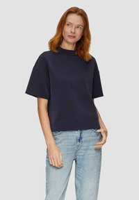 Marineblaues, kurzärmeliges Cropped-T-Shirt mit hohem Ausschnitt, glatter Textur und lässiger Passform, kombiniert mit hellblauen, ausgebeulten Jeans.