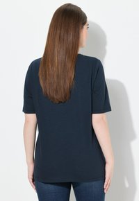 Top de manga corta azul marino hecho de tela suave, con una forma relajada y cuello redondo, combinado con jeans azul oscuro.