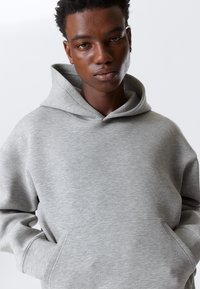 Grijze hoodie gemaakt van een zachte katoenmix. Voorzien van een voorzak, een ruime capuchon en een ontspannen pasvorm met een subtiele structuur.