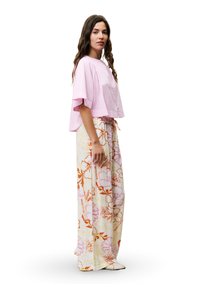 Roze linnen crop top met knoopdetails; wijdlopende bloemenbroek in geel, roze en oranje. Vloeiende, lichte stof en trekkoord taille.