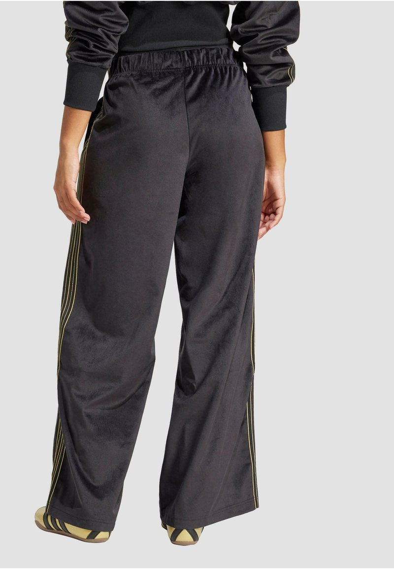 Pantaloni da corsa in velluto nero con un design a gamba larga, caratterizzati da strisce laterali dorate e una vita elasticizzata per il massimo comfort.
