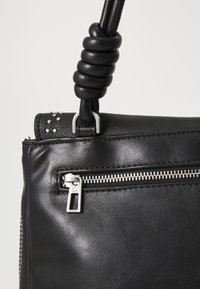 Black leather handbag with a zippered pocket, stud accents, and a coiled handle detail. Smooth texture and silver hardware featured.