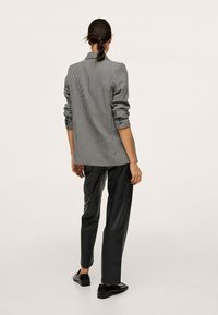 Szara i biała marynarka w kratę z podwiniętymi rękawami i luźnym krojem, zestawiona z czarnymi skórzanymi spodniami i czarnymi butami.