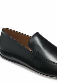 Mocassin en cuir noir à enfiler avec une tige lisse et un détail de couture subtil sur fond blanc.