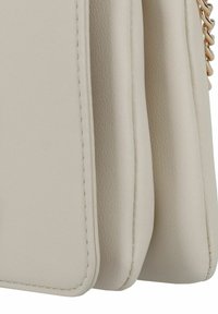 Borsa a tracolla in pelle beige con un design strutturato, caratterizzata da cuciture visibili e un accento di catena. Texture liscia con un profilo elegante.