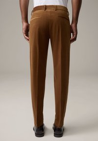 Bruine corduroy broeken met een rechte pasvorm, voorzien van twee achterzakken en een gladde textuur. Gecombineerd met zwarte schoenen.