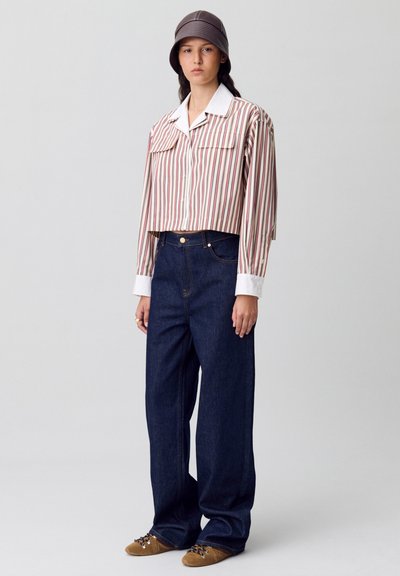 Camisa a rayas cortada con cuello blanco, jeans de mezclilla oscuros de pierna ancha y zapatos marrones. El modelo lleva un sombrero tipo cubo marrón. Diseño simple.