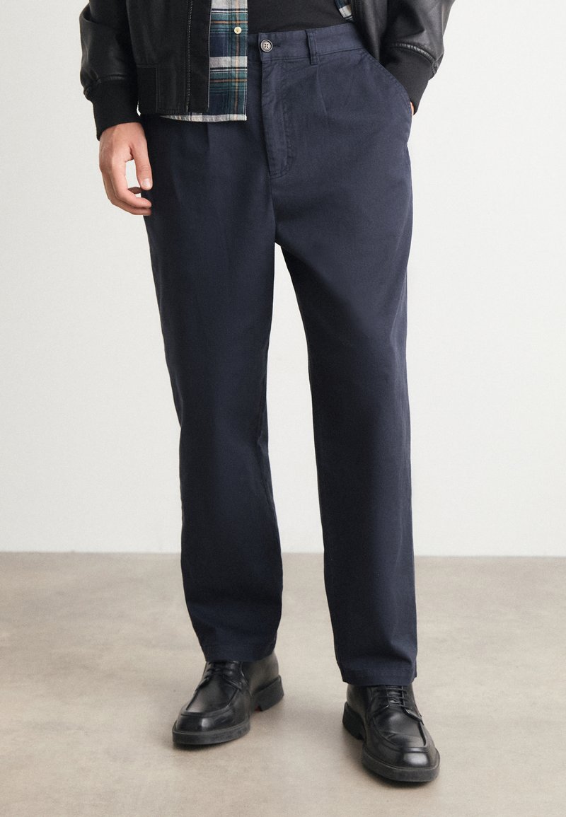 Navyblauwe katoenen broek met een relaxed fit, voorzien van zijzakken, een knoopsluiting en gedragen met zwarte leren schoenen.