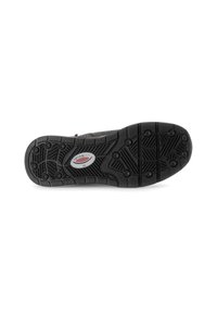 Semelle de chaussure en caoutchouc noir avec une surface texturée, présentant un motif de semelle pour traction et une étiquette de logo centrale.