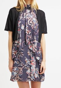 Blommönstrad klänning i mörkblått med rosa, röd och vita accenter, ihop med en kort svart cardigan. Lätt och flödande tyg.