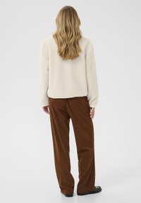 Ecrufarbene Fleecejacke mit einer lässigen Passform, kombiniert mit braunen Cordhosen. Die Hosen haben eine gerippte Textur und weite Beine.