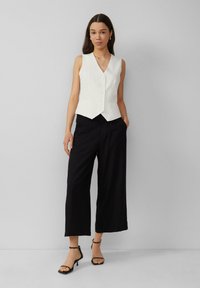 White pinstripe sleeveless vest with a v-neck and front buttons, paired with loose black wide-leg trousers and black strappy heels.