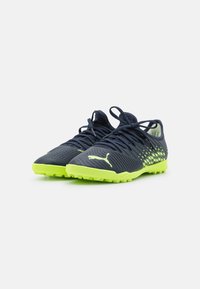 Football shoes made of synthetic material, featuring a navy upper with a green sole, textured design, and tonal lacing.