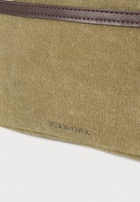 Τσάντα από χακί καμβά με καφέ δερμάτινη λεπτομέρεια. Διαθέτει ανάγλυφο λογότυπο "Pier One", υφή επιφάνειας και μινιμαλιστικό σχεδιασμό.