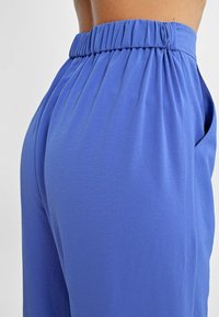 Pantaloni azzurri chiari, larghi, con una vita elasticizzata arricciata, realizzati in un tessuto morbido e texturizzato, dotati di tasche laterali.