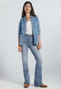 Ljus denimskjorta med fickor, bärs över en vit topp; kombineras med högmidjade ljusblå utsvängda jeans och bruna ankelboots.