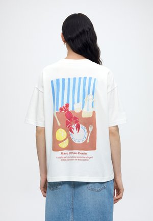 Πίσω μέρος λευκού πουκαμίσου με πολύχρωμες αστακοκαραβίδες, λεμόνι, πιάτο, πιρούνι, κανάτα και μπλε ριγέ φόντο, φορεμένο από ένα άτομο με μακριά σκουρόχρωμα μαλλιά.