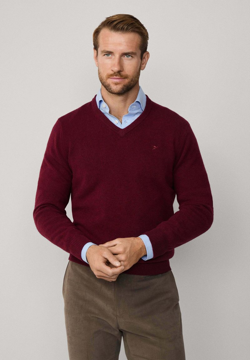 Pull en maille bordeaux à col en V avec des poignets et un ourlet côtelé, associé à une chemise à col bleu clair en dessous. Texture lisse, coupe décontractée.