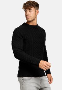Schwarzer Strickpullover mit strukturiertem Muster, Rundhalsausschnitt und gerippten Bündchen und Saum. Das Material wirkt dick und warm.