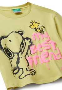 Žluté tričko s černým obrysem Snoopyho a Woodstocaka s růžovým textem "můj nejlepší přítel" na přední straně.